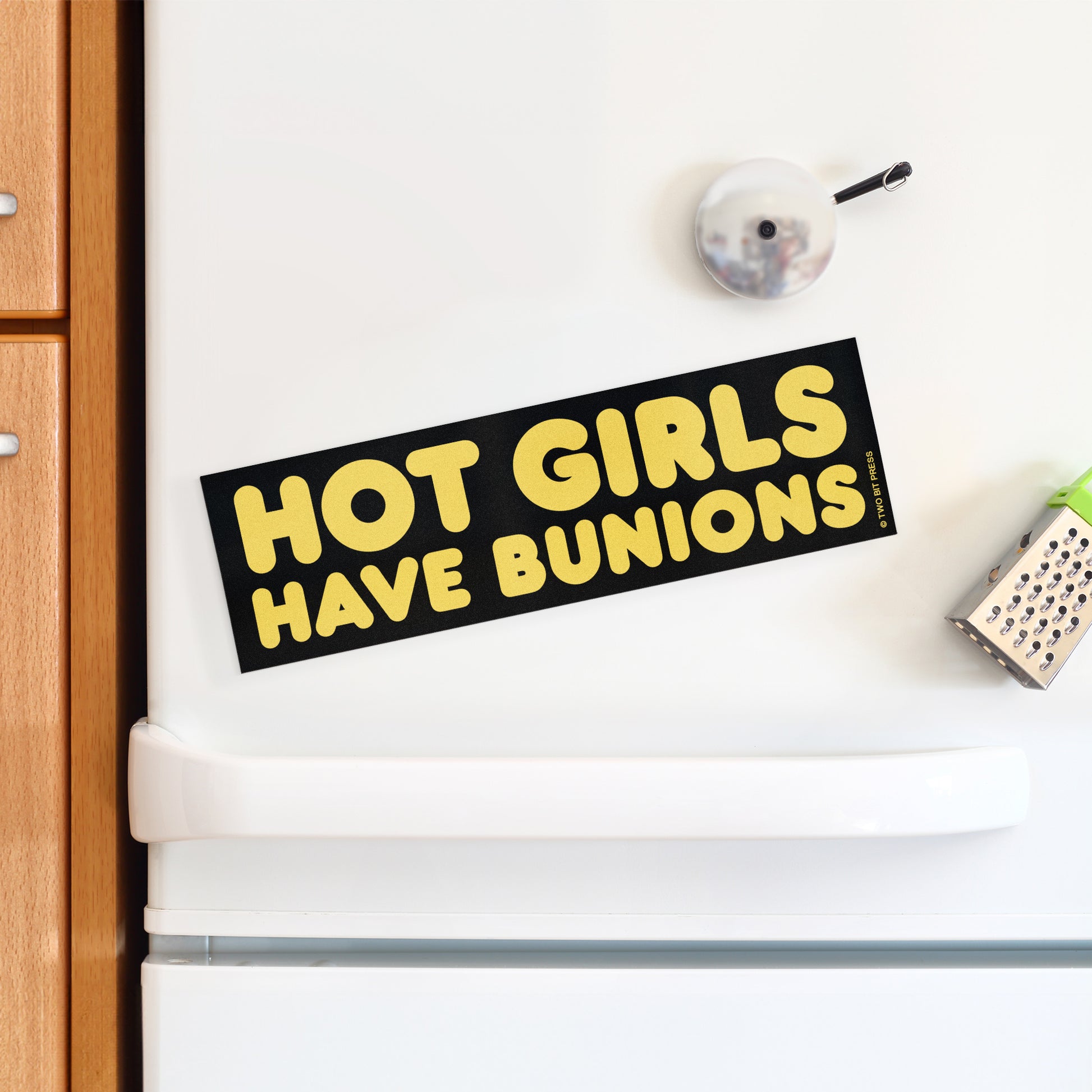 A vinyl bumper magnet reading "HOT GIRLS HAVE BUNIONS" on a white fridge.