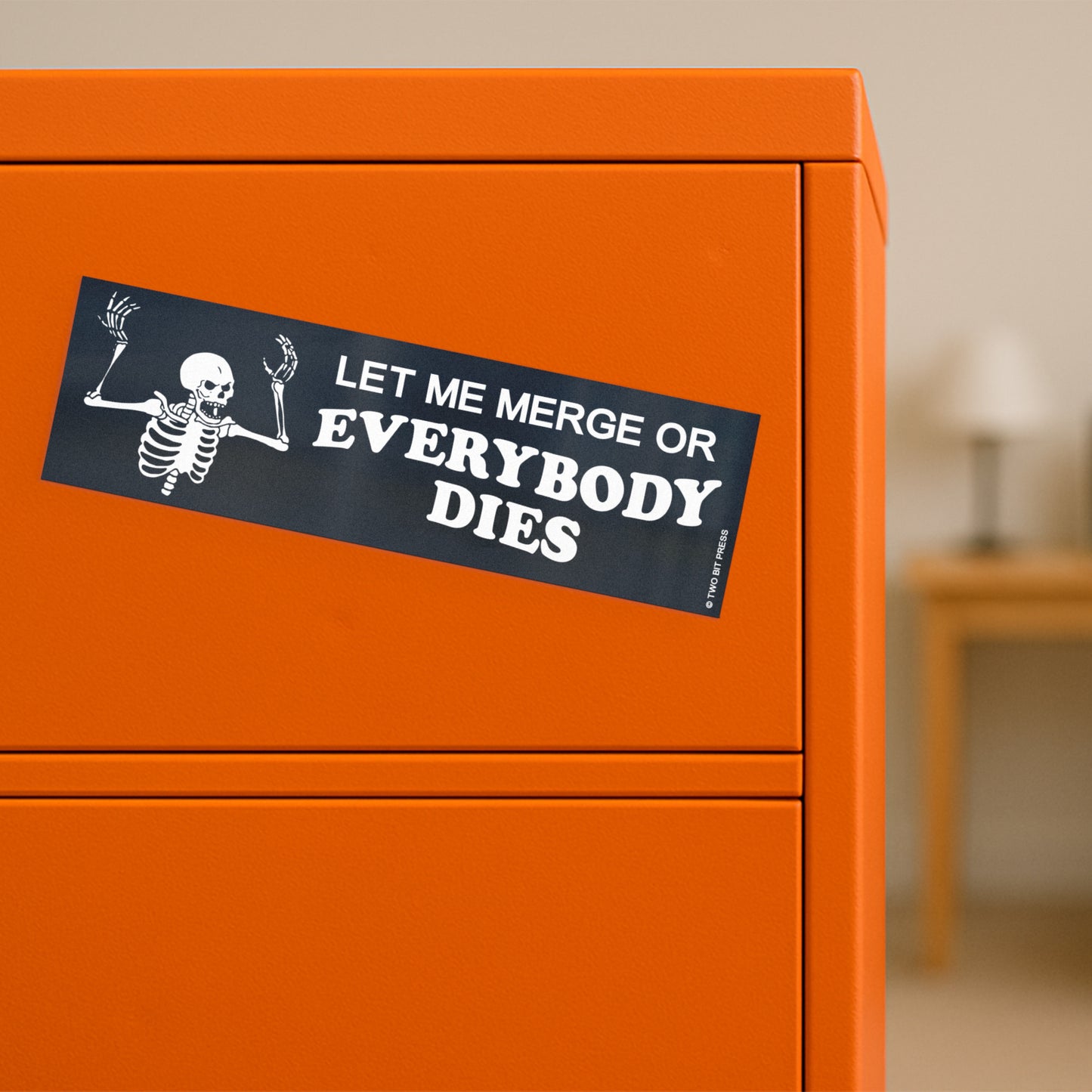 A vinyl bumper magnet showing an angry skeleton, with the text  "LET ME MERGE OR EVERYBODY DIES" on orange filing cabinet.