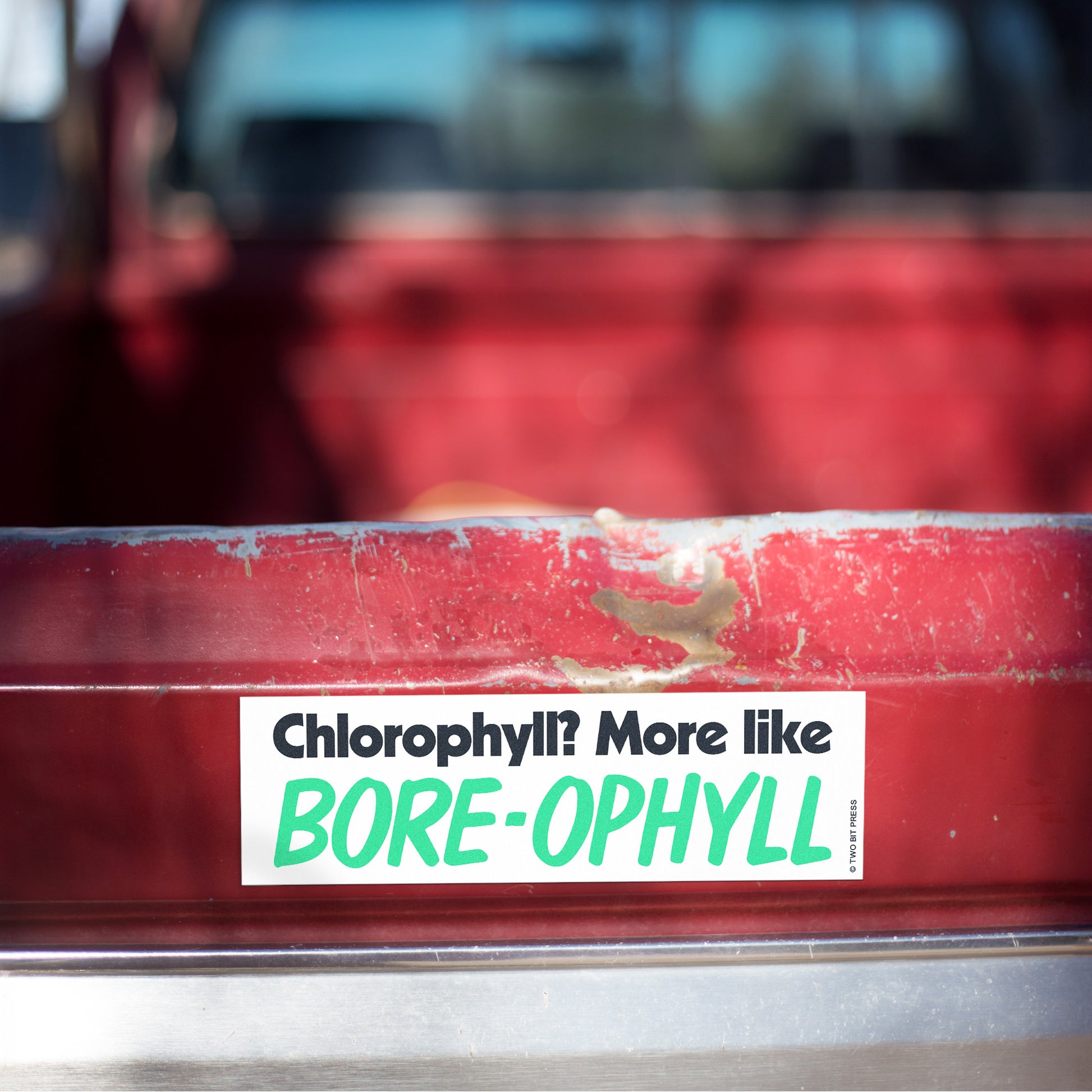 A vinyl bumper magnet reading "Chlorophyll? More like BORE-OPHYLL" on red truck tailgate.