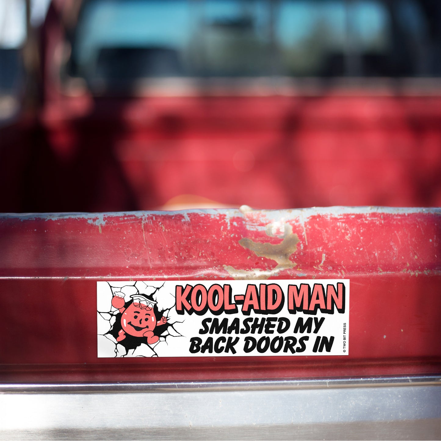 A vinyl bumper magnet showing the Kool-Aid Man and the text "KOOL-AID MAN SMASHED MY BACK DOORS IN" on red truck tailgate.