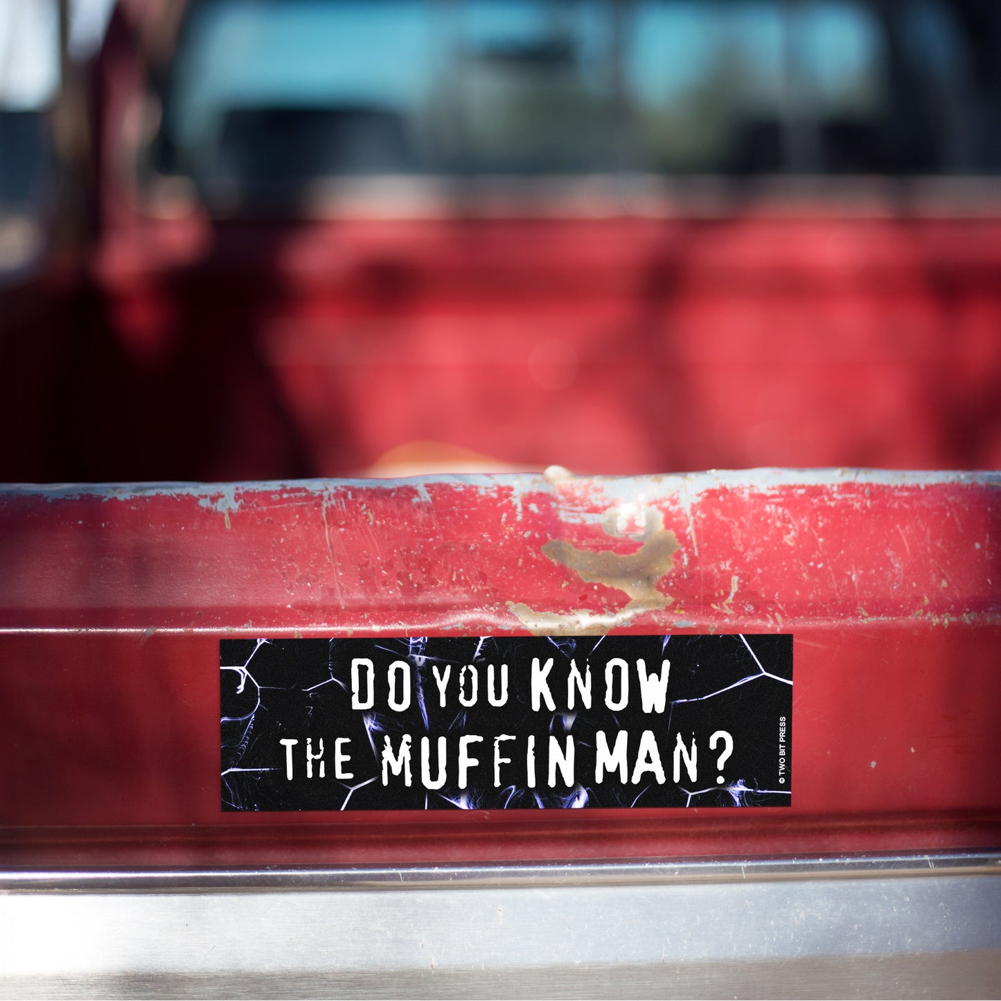 A vinyl bumper magnet reading "DO YOU KNOW THE MUFFIN MAN?" on red truck tailgate.
