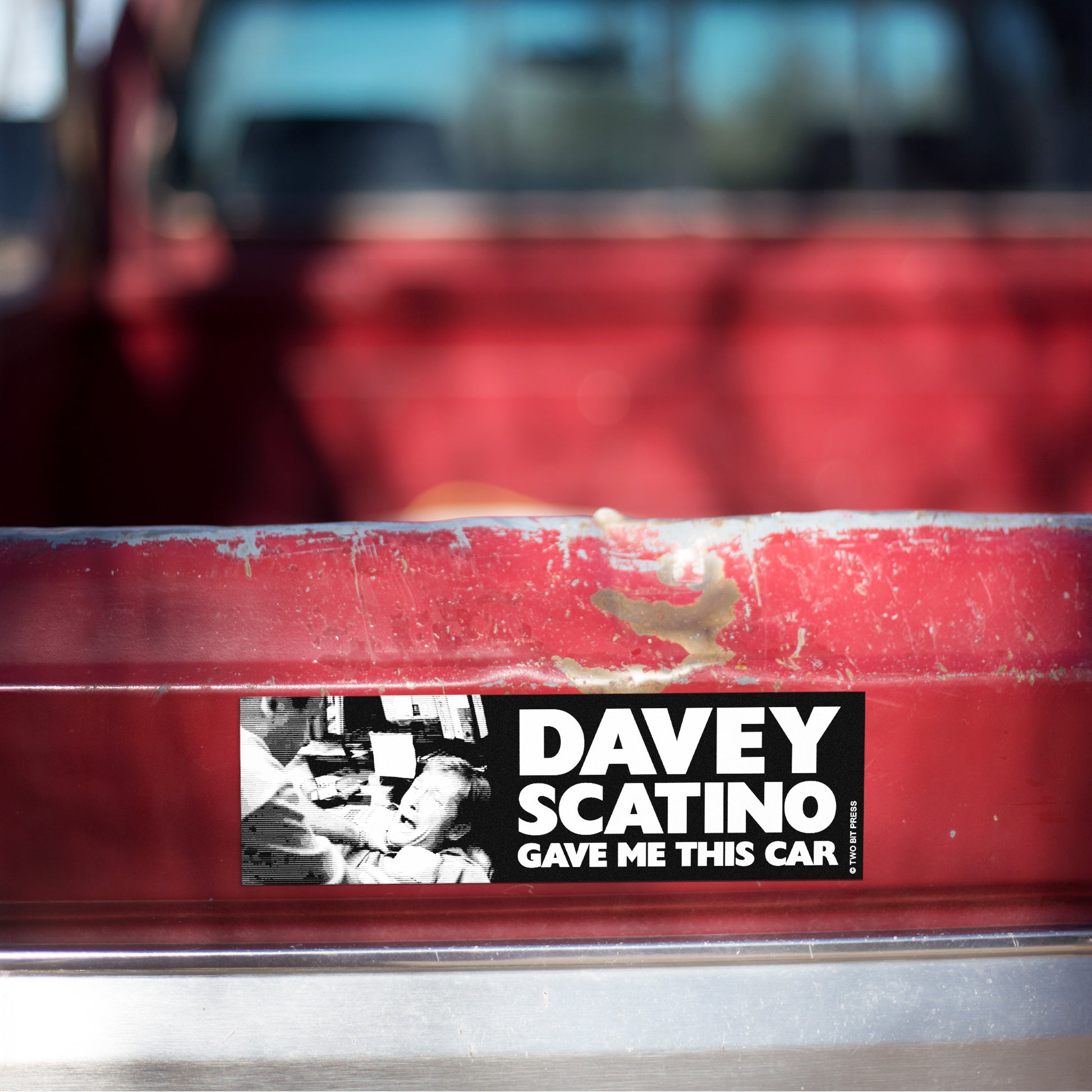 A vinyl bumper magnet showing the Sopranos and the text "DAVEY SCATINO GAVE ME THIS CAR" on red truck tailgate.