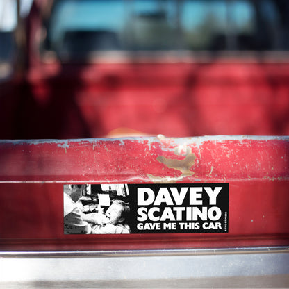 A vinyl bumper magnet showing the Sopranos and the text "DAVEY SCATINO GAVE ME THIS CAR" on red truck tailgate.
