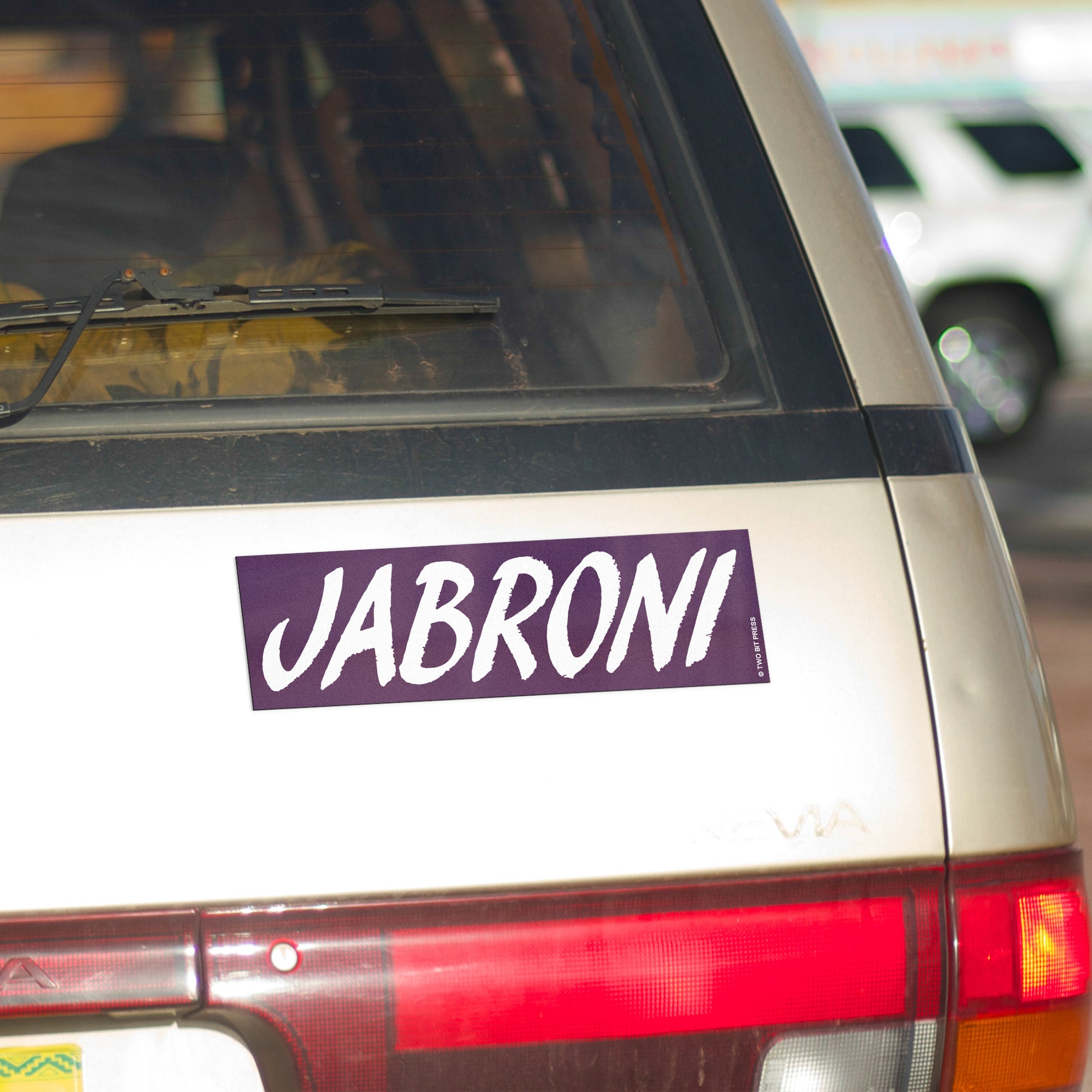 A vinyl bumper magnet reading "JABRONI" on gold minivan.