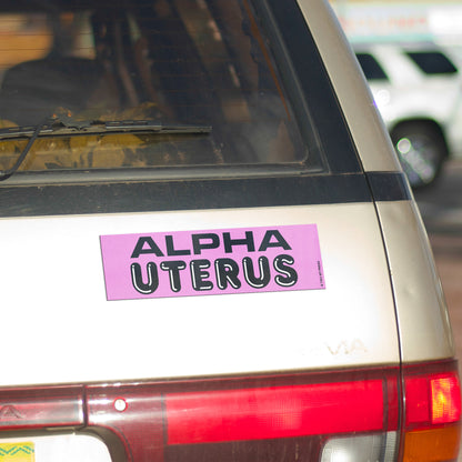 A vinyl bumper magnet reading "ALPHA UTERUS" on gold minivan.