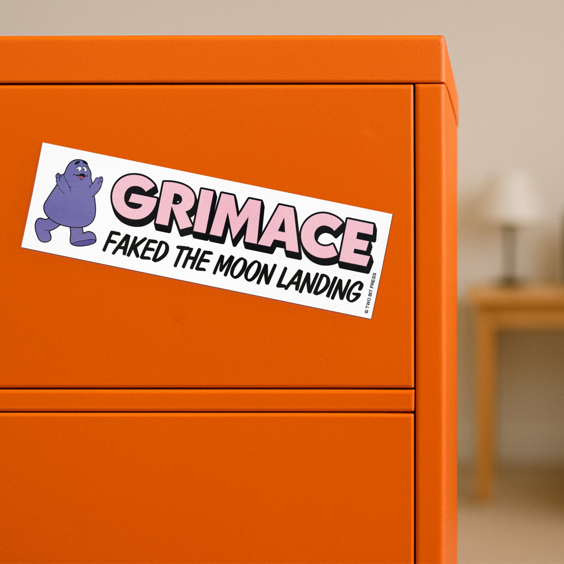 A vinyl bumper magnet showing Grimace and the text "GRIMACE FAKED THE MOON LANDING" on orange filing cabinet.