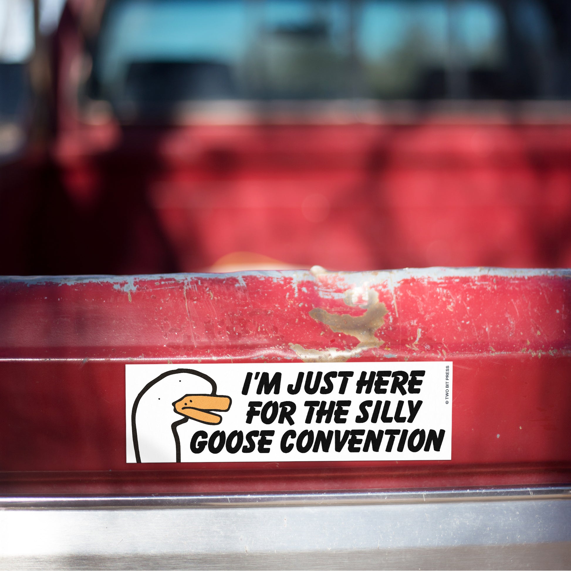 A vinyl bumper magnet showing a goose and the text "I'M JUST HERE FOR THE SILLY GOOSE CONVENTION" on red truck tailgate.