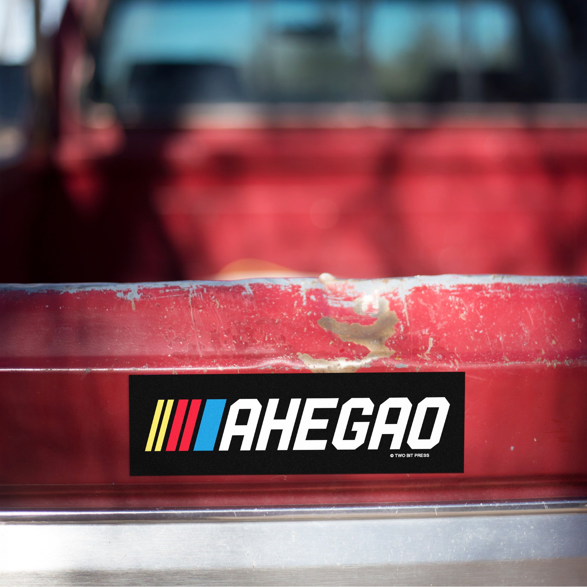 A vinyl bumper magnet reading "AHEGAO" on red truck tailgate.