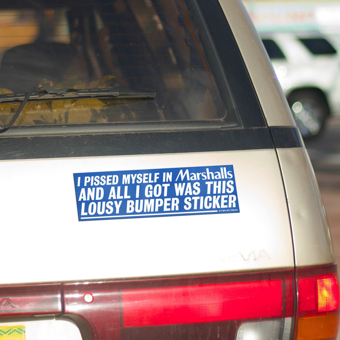 A bumper magnet reading "I PISSED MYSELF IN Marshalls AND ALL I GOT WAS THIS LOUSY bumper magnet" on gold minivan.