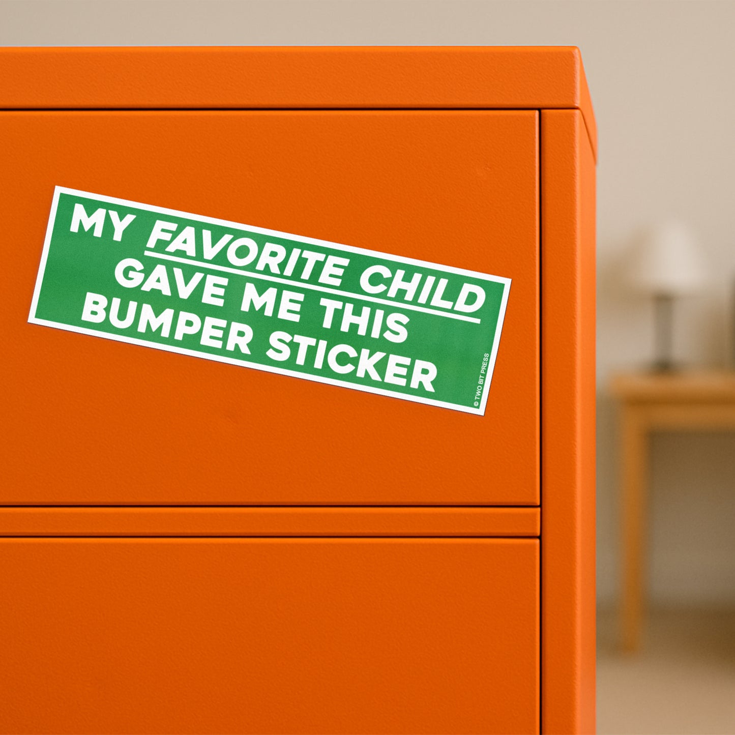 A vinyl bumper magnet reading "MY FAVORITE CHILD GAVE ME THIS bumper magnet" on orange filing cabinet.