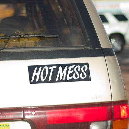 A vinyl bumper magnet reading "HOT MESS" on gold minivan.