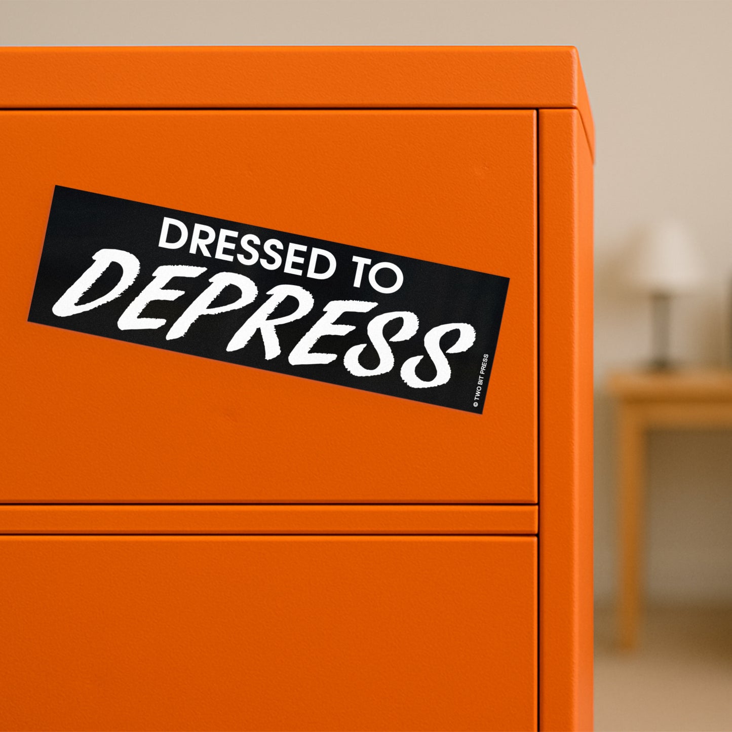 A vinyl bumper magnet reading "DRESSED TO DEPRESS" on orange filing cabinet.
