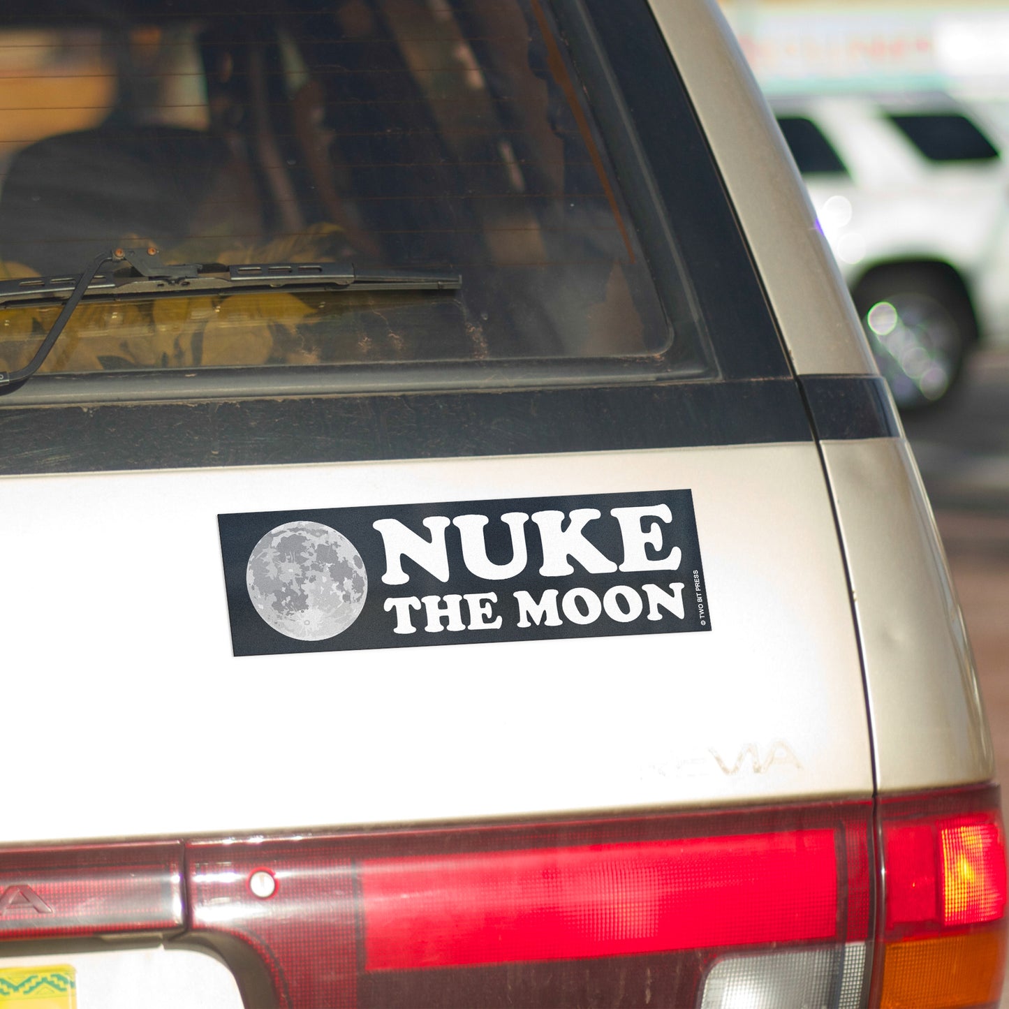 A vinyl bumper magnet showing the moon and the text "NUKE the MOON" on gold minivan.