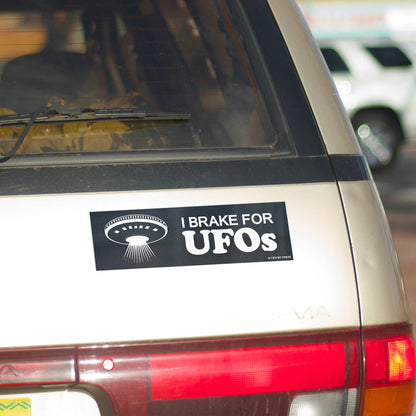 A vinyl bumper magnet showing a flying saucer and the text "I BRAKE FOR UFOS" on gold minivan.
