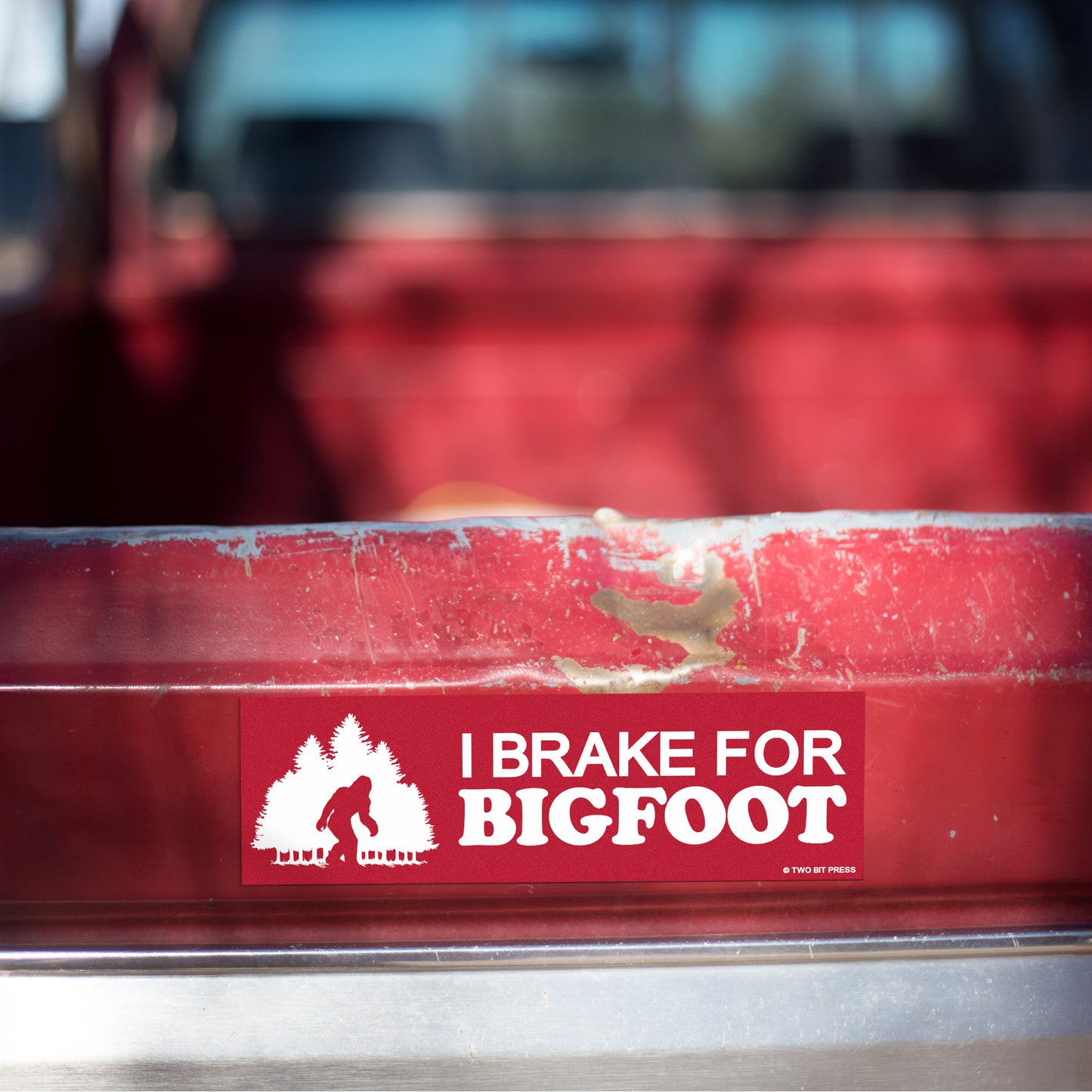 A vinyl bumper magnet showing a sasquatch and the text "I BRAKE FOR BIGFOOT" on red truck tailgate.