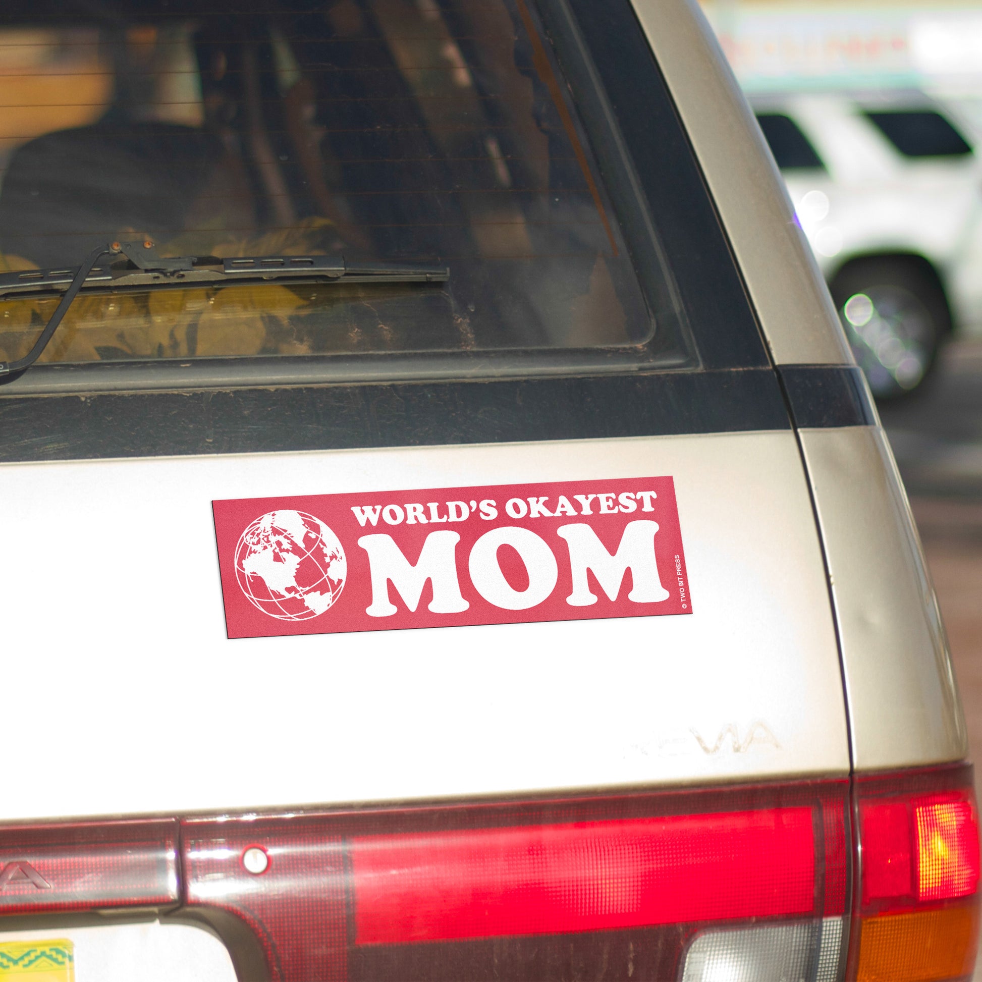 A vinyl bumper magnet showing a globe and the text "WORLD'S OKAYEST MOM" on gold minivan.