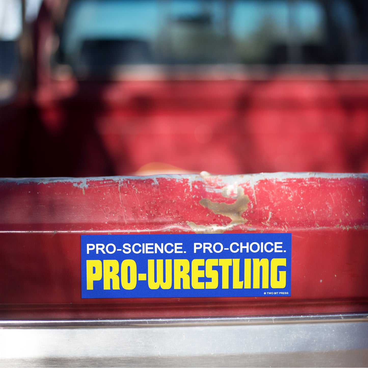 A vinyl bumper magnet reading "PRO-SCIENCE. PRO-CHOICE. PRO-WRESTLING" on red truck tailgate.