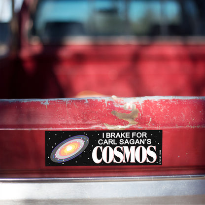 A vinyl bumper magnet showing a galaxy graphic and the text "I BRAKE FOR CARL SAGAN'S COSMOS" on red truck tailgate.