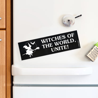 A vinyl bumper magnet showing a witch on a broomstick with the text "WITCHES OF THE WORLD, UNITE" on a white fridge.
