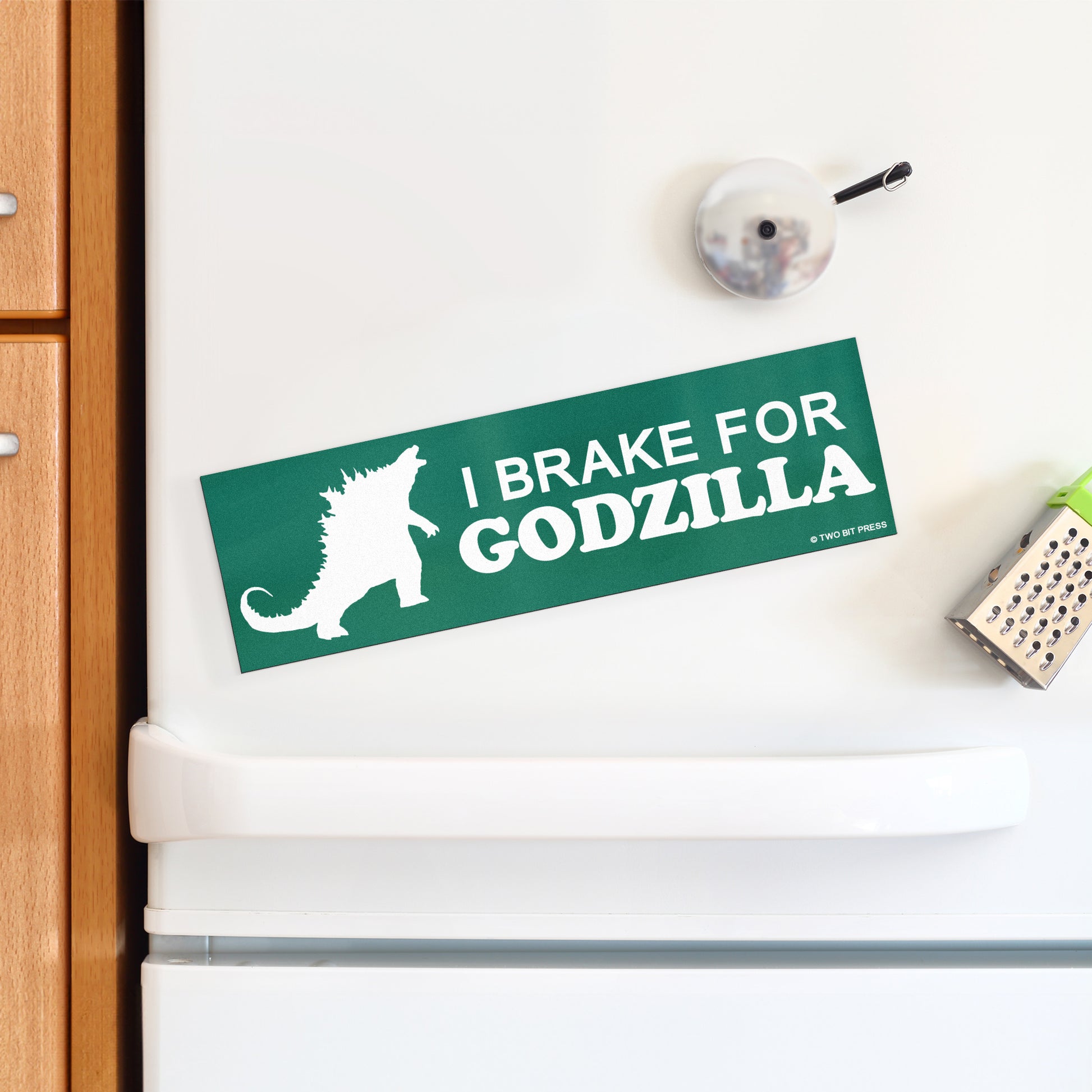 A vinyl bumper magnet showing Godzilla and the text "I BRAKE FOR GODZILLA" on a white fridge.