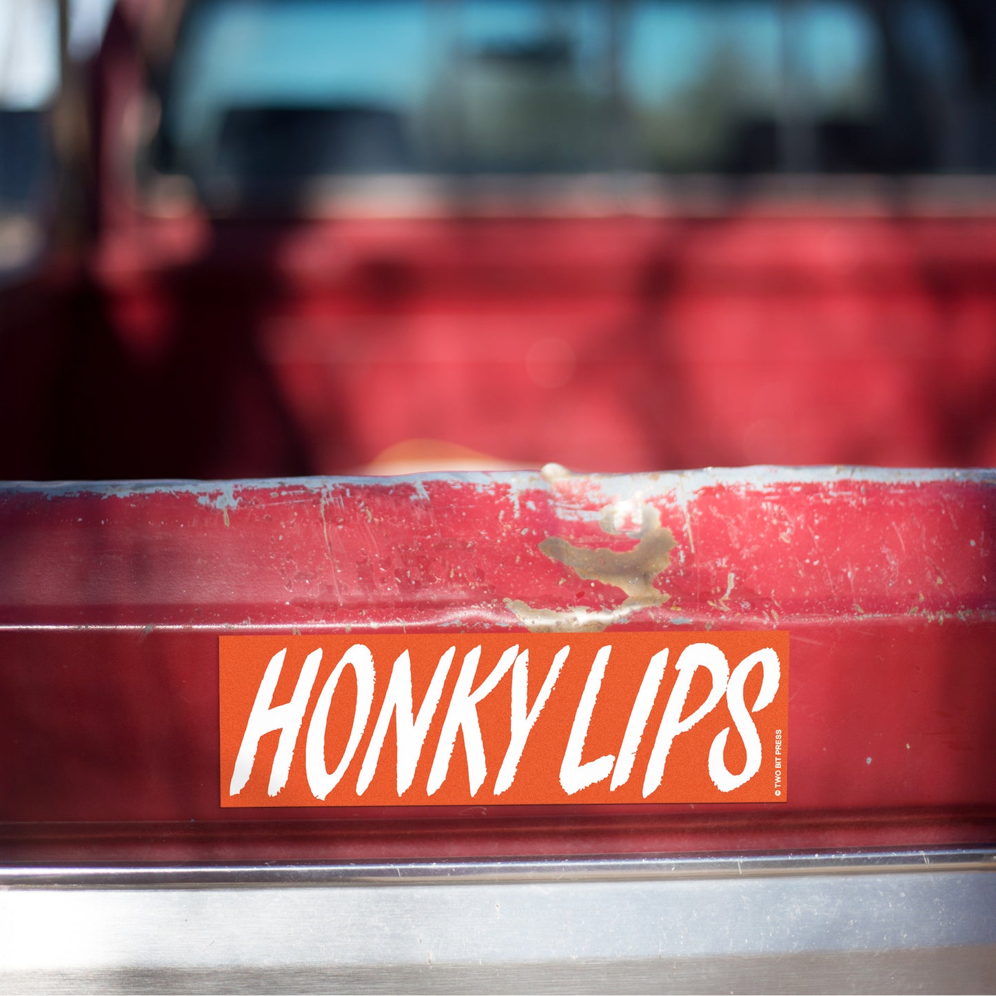 A vinyl bumper magnet reading "HONKY LIPS" on red truck tailgate.