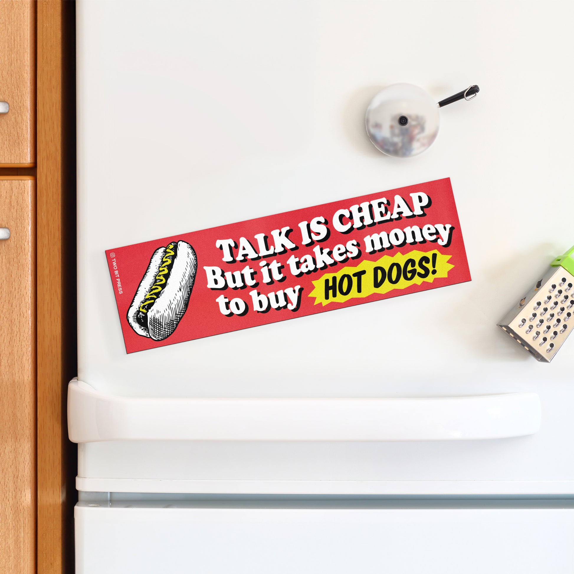 A bumper magnet showing a hot dog and the text "TALK IS CHEAP But it takes money to buy HOT DOGS!" on a white fridge.