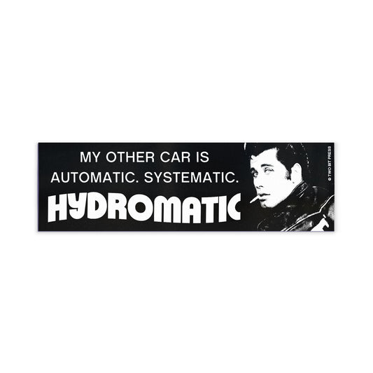 A bumper magnet showing John Travolta and the text "MY OTHER CAR IS AUTOMATIC SYSTEMATIC HYDROMATIC" on a white background.