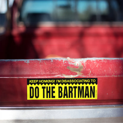 A vinyl bumper magnet reading "KEEP HONKING! I'M DISASSOCIATING TO DO THE BARTMAN" on red truck tailgate.