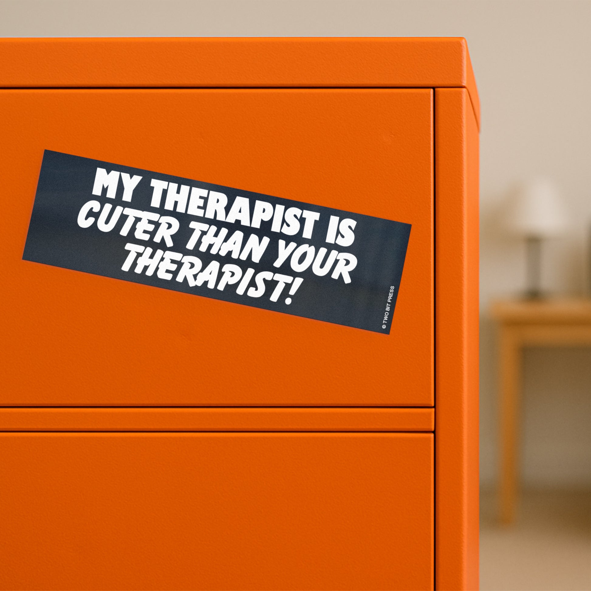 A vinyl bumper magnet reading "MY THERAPIST IS CUTER THAN YOUR THERAPIST!" on orange filing cabinet.